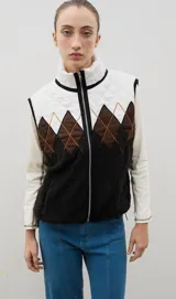 Chaleco con cierre frontal y cuello alto, que combina una parte superior acolchada con diseño de rombos en tonos blanco y marrón, y una parte inferior de corderito negro.
