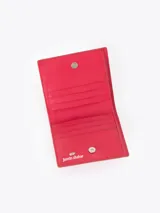 Mini billetera de cuero vacuno color rojo, con diseño grabado de pequeñas mariquitas en el frente y un aplique metálico en forma de corazón. Cuenta con un interior funcional con espacios organizadores para tarjetas.