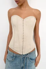 Top tipo corset de escote corazón y hombros descubiertos, con varillas interiores para estructura. Presenta cierre frontal con ganchos metálicos y ajuste en la espalda mediante cordones cruzados.