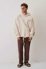 Hoodie de felpa color beige, con capucha, bolsillo frontal tipo canguro y pequeño logo de la marca estampado en el pecho.