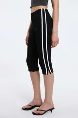 Pantalón capri negro de corte ajustado, con cintura elástica y franjas blancas decorativas en los laterales.