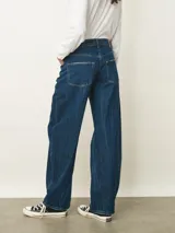 Jean de corte recto y tiro medio, con un acabado de lavado oscuro y efecto de textura sutil en la tela. Presenta cierre frontal con botón y bolsillos clásicos.