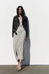 Cazadora biker negra de efecto piel, con cuello solapa, manga larga con trabillas en hombros, bolsillos delanteros con cierre de cremallera, bajo acabado con cinturón a tono con hebilla metálica y cierre frontal cruzado con cremallera.