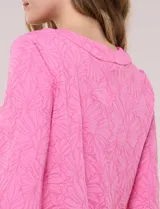 Blusa rosada con textura en relieve de motivos florales, cuello redondo con pequeña muesca y mangas tres cuartos.