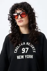 Buzo negro de corte holgado con estampado frontal que dice "Chelsea Heights 97 New York".