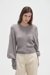 Saco de punto color beige, con cuello redondo, cierre frontal con botones y mangas largas con puños acanalados.