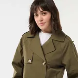 Trench corto de color verde militar, con diseño de doble botonadura, solapas anchas y trabillas en los hombros. Presenta un corte estructurado y mangas largas.