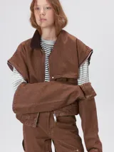 Campera de denim a rayas verticales con cuello de pana en color bordó. Presenta cierre frontal, mangas desmontables con cierre en los hombros, canesú en el pecho y bolsillos de parche cuadrados.