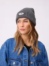 Gorro tipo beanie de tejido acanalado con diseño a rayas verticales en tonos azul y gris. Presenta un parche frontal con el logo de la marca Rusty.