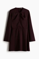 Vestido corto de color bordó, con escote redondo y detalle girado en el frente. Presenta mangas largas con abertura en los puños, falda con leve vuelo y cierre oculto en la espalda.