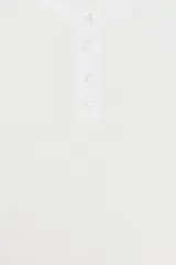 Vestido corto blanco con cuello redondo y manga larga tipo murciélago. El bajo tiene un acabado voluminoso con tejido combinado a tono y cierre frontal con botones.