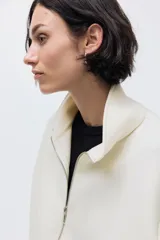 Campera color crema con efecto neopreno, cuello chimenea y cierre frontal. Presenta hombros caídos y pliegues en el bajo.