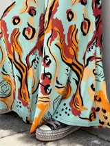 Pantalón palazzo de tiro alto con estampado abstracto en tonos naranja, rojo y negro sobre fondo celeste.