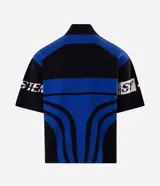 Remera de tricot liviano Blue Steel con corte boxy, cuello polo alto y cierre frontal parcial de un cuarto. Presenta diseño jacquard integral con gráficos y lettering en tonos azul, negro y blanco, mangas cortas y estilo de inspiración deportiva.