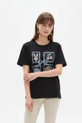 Remera negra de algodón con cuello redondo, mangas cortas y calce holgado. Cuenta con un estampado frontal estilo collage con ilustraciones en relieve de motivos marinos y frutales, unidas por un lazo.