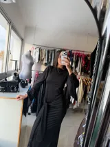 Vestido largo negro de corte ajustado, con mangas largas acampanadas y detalle de nudo frontal en la cintura que crea un efecto drapeado.