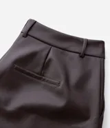 Pantalón de cuero sintético con corte barrel, de tiro alto y pierna ancha con estructura curva. Presenta bolsillos laterales tipo cuchillo y costuras decorativas con pespuntes visibles.