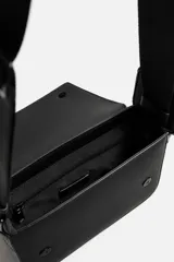 Bandolera negra con acabado engomado y textura de líneas horizontales. Tiene un compartimento principal con cierre de solapa y botón a presión, un bolsillo interior con cremallera y un asa de hombro ajustable con monedero cuadrado.