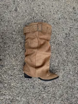 Botas altas de gamuza color beige, con diseño slouchy, punta fina y una tira ancha superior con hebilla metálica rectangular y ojalillos.