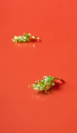 Aro tipo argolla dorada con colgante en forma de racimo de uvas, compuesto por pequeñas cuentas de cristal verde y hojas metálicas doradas.