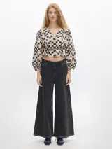 Blusa crop de denim con estampado a cuadros en tonos beige y negro, de manga larga abullonada con puños elásticos y escote en V.
