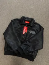Campera de cuero sintético negro con diseño tipo bomber, cuello camisero y puños y ruedo elásticos. Presenta un bordado grande en la espalda con tipografía cursiva en color blanco.