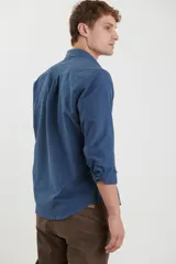 Camisa de vestir blanca de manga larga, con cuello abotonado, bolsillo frontal y botones en tono madera.