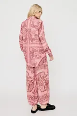 Camisa oversize rosada con estampado de mariposas y motivos florales, de manga larga y cierre frontal de botones.