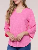 Blusa rosada con textura en relieve de motivos florales, cuello redondo con pequeña muesca y mangas tres cuartos.