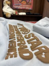 Hoodie de color celeste con capucha y diseño estampado en relieve en la espalda con texto en color marrón. Presenta un corte holgado y cómodo.