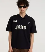 Remera de corte boxy confeccionada en algodón, con cuello polo y cierre frontal de botones. Presenta un diseño estampado en el frente con el número 93, una cruz y la palabra MAD en tipografía gótica.