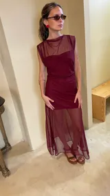 Vestido largo de microtul bordó, sin mangas, con escote alto tipo buche y diseño transparente con forro corto interno que genera un efecto translúcido en la falda.