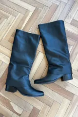 Bota de caña alta confeccionada en cuero vacuno, con diseño de caña holgada y taco cuadrado bajo. Cuenta con cierre interno para facilitar su colocación.