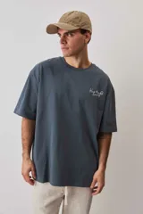 Remera oversize azul con mangas anchas, cuello redondo con textura tejida y estampa frontal pequeña a la altura del pecho.