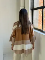 Poncho de punto con diseño de rayas horizontales en tonos tierra, blanco y beige. Presenta un corte holgado, cuello redondo y mangas anchas con puños acanalados.