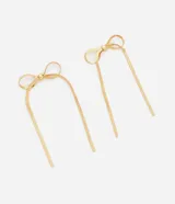 Caravanas de metal dorado con diseño de lazo de cinta italiana y extremos largos colgantes. Cuentan con cierre de tornillo y están confeccionadas en latón.