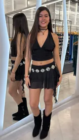 Minifalda short de tiro bajo color negro, con diseño de volados en cascada y una faja de cadera decorada con apliques metálicos circulares plateados.