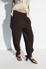 Pantalón bombacho de tiro alto, color marrón, con efecto arrugado y cintura elástica en la espalda. Cuenta con pinzas delanteras, bolsillos frontales, pernera abullonada y puños acabados en lazo.