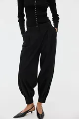 Pantalón negro de tiro medio con corte holgado y diseño de piernas globo, pinzas en la parte delantera y puños elásticos ajustados en los tobillos. Cuenta con cierre frontal y trabillas para cinturón.