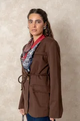 Chaquetón color beige de corte recto y largo, con cierre frontal mediante botones y lazo ajustable en la cintura. Presenta cuello en V, bolsillos laterales con solapa y mangas largas.