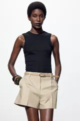 Bermuda color crema de tiro medio con pinzas delanteras y cinturón fino color beige. Tiene bolsillos frontales y falsos bolsillos de vivo en la espalda. Cierre frontal con cremallera, botón interior y gancho.