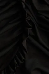 Vestido corto negro de manga larga con escote redondo. Presenta secciones drapeadas y fruncidas en el torso y el bajo, con ribetes de volados a lo largo de los bordes del drapeado y en los puños.