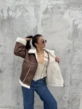 Campera tipo gamulán color marrón, con interior y detalles en corderito blanco. Presenta cierre frontal, cuello solapa y bolsillos laterales.