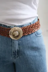 Cinto de cuero trenzado color marrón chocolate, con hebilla circular metálica grabada y detalle central de piedra natural.