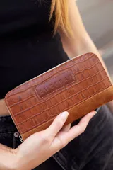 Billetera mediana marrón de cuero con textura croco y detalles en gamuza. Tiene cierre perimetral y logo Austera grabado en el frente.