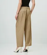 Pantalón de sastrería de crepé color marrón, de corte carrot, con pliegues delanteros, pinzas, bolsillos laterales y cierre frontal.
