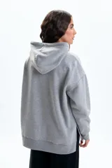 Canguro deportivo de corte holgado en color gris melange, con capucha ajustable mediante cordones y mangas largas con puños acanalados.