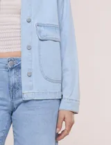Campera de denim blanco de corte holgado con hombros caídos, cuello con solapa en contraste de color celeste, cierre frontal con botones metálicos y bolsillos delanteros con solapa.