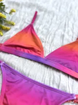 Conjunto de bikini con corpiño triangular fijo y bombacha colaless regulable, con estampado degradado en tonos naranja, rosado y violeta.