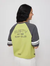 Remera bicolor Rusty de corte holgado y estilo deportivo, con cuerpo blanco y mangas raglán azules con doble raya blanca. Presenta estampado frontal con el texto 'RUSTY 85'.